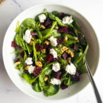 beet and goat cheese salad in a white bowl with a fork and breadcrumbs on the table