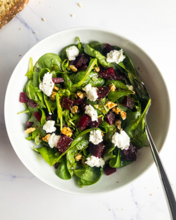beet and goat cheese salad in a white bowl with a fork and breadcrumbs on the table