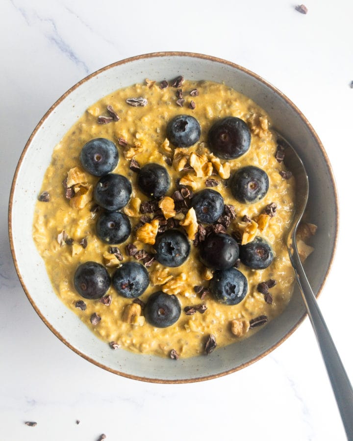 pumpkin pie overnight oats with blueberries and walnuts in a bowl with a spoon