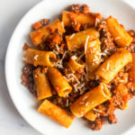 rigatoni bolognese on a white plate with a fork