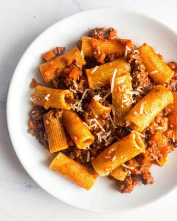 rigatoni bolognese on a white plate with a fork