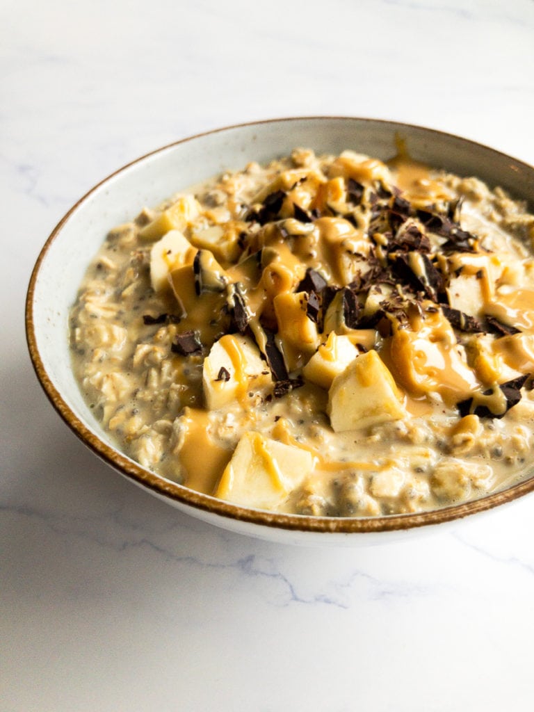peanut butter overnight oats in a bowl, topped with banana, chocolate chunks and a drizzle of peanut butter