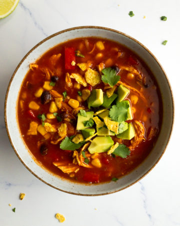 spicy Mexican chicken soup in a bowl, topped with avocado and cilantro