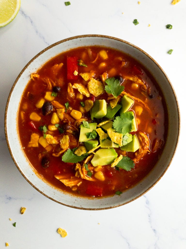 spicy Mexican chicken soup in a bowl, topped with avocado and cilantro