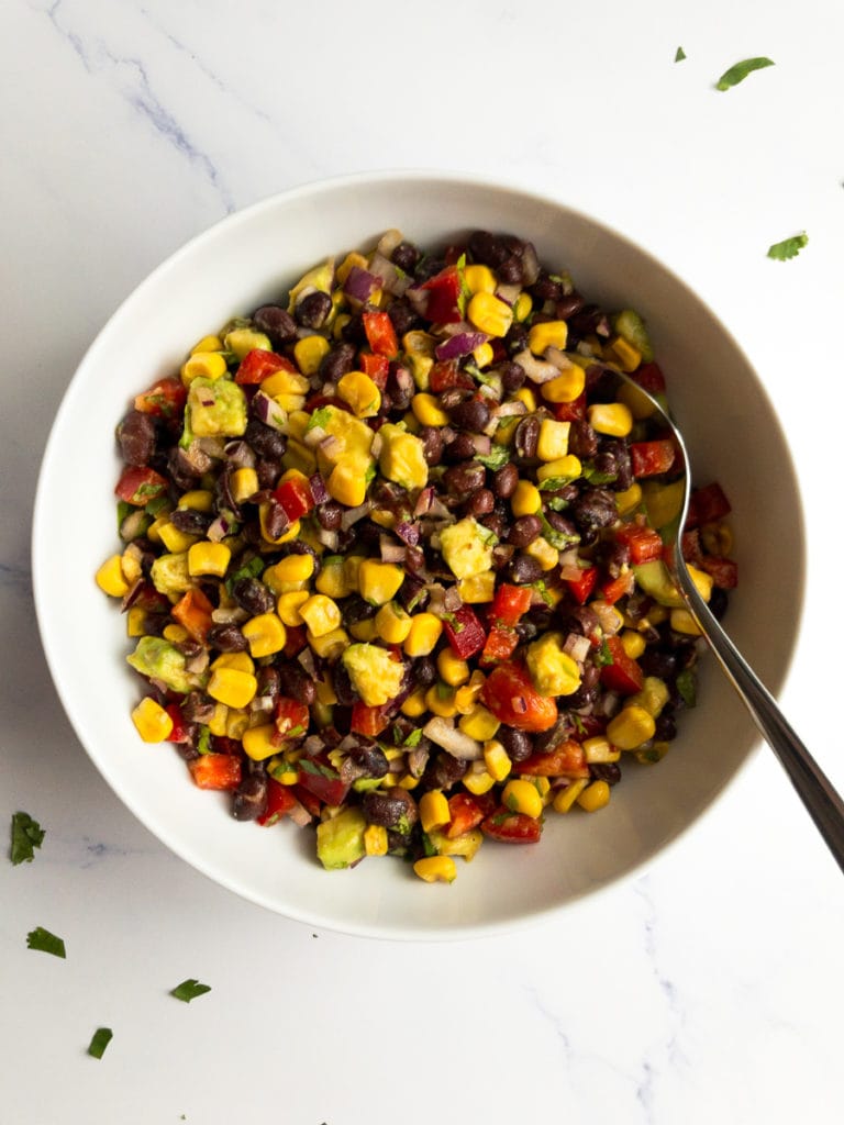 black bean and corn salad in a white bowl with a spoon