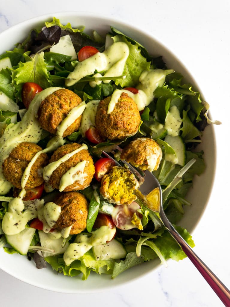 falafel over a bed of greens and avocado lime dressing drizzled on top