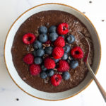 chocolate chia seed pudding topped with blueberries and raspberries in a bowl with a spoon