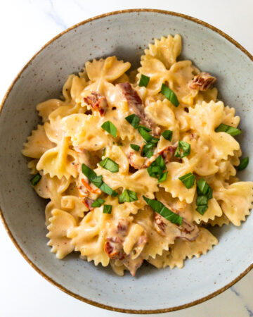 creamy sun-dried tomato pasta garnished with fresh basil leaves in a bowl