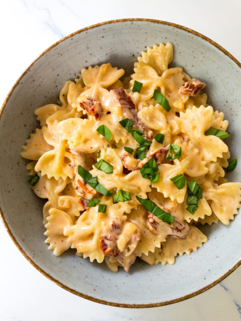 creamy sun-dried tomato pasta garnished with fresh basil leaves in a bowl
