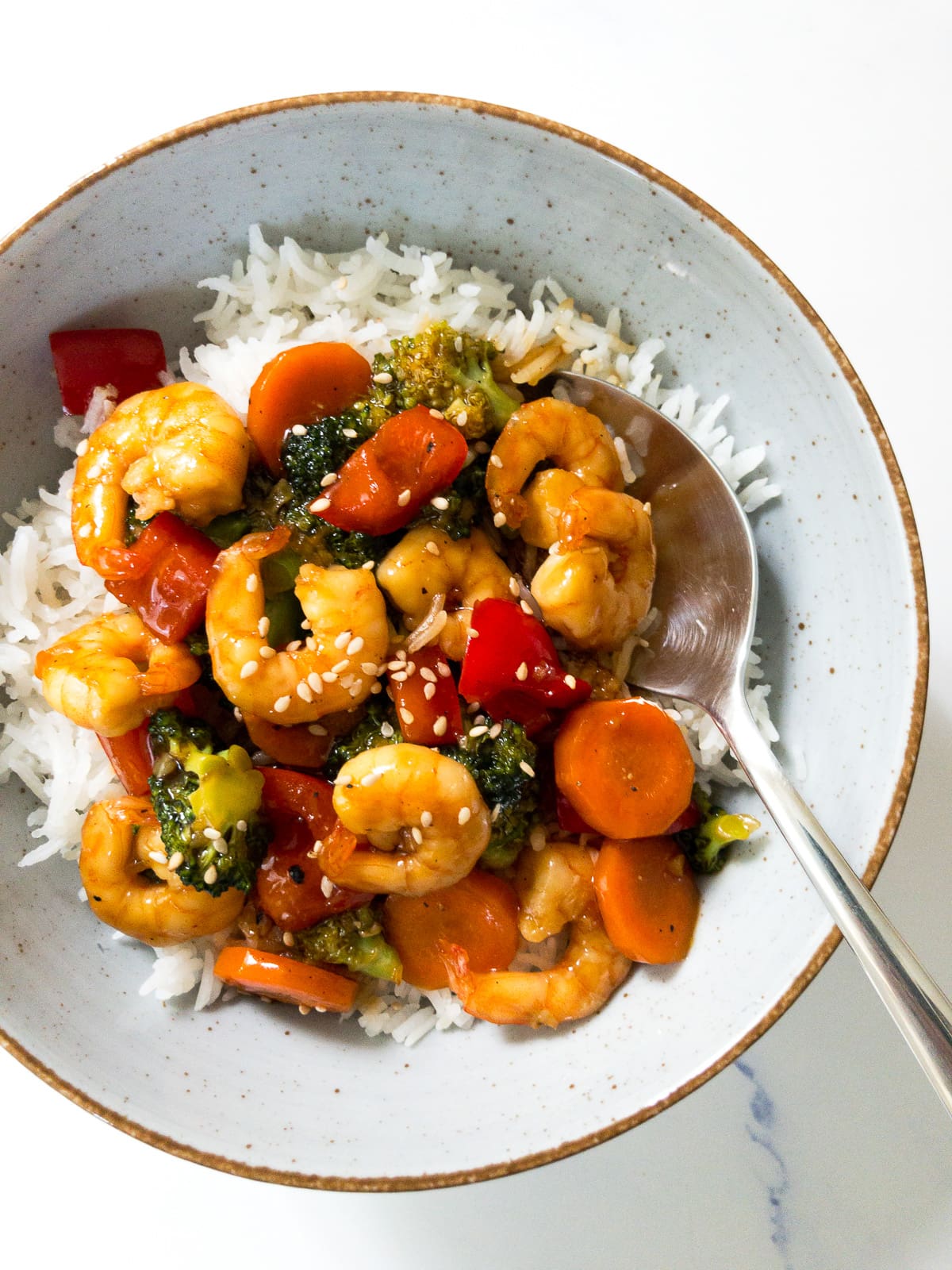 teriyaki shrimp stir fry served over white rice in a bowl and a spoon