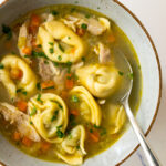 chicken tortellini soup garnished with parsley in a bowl with a spoon