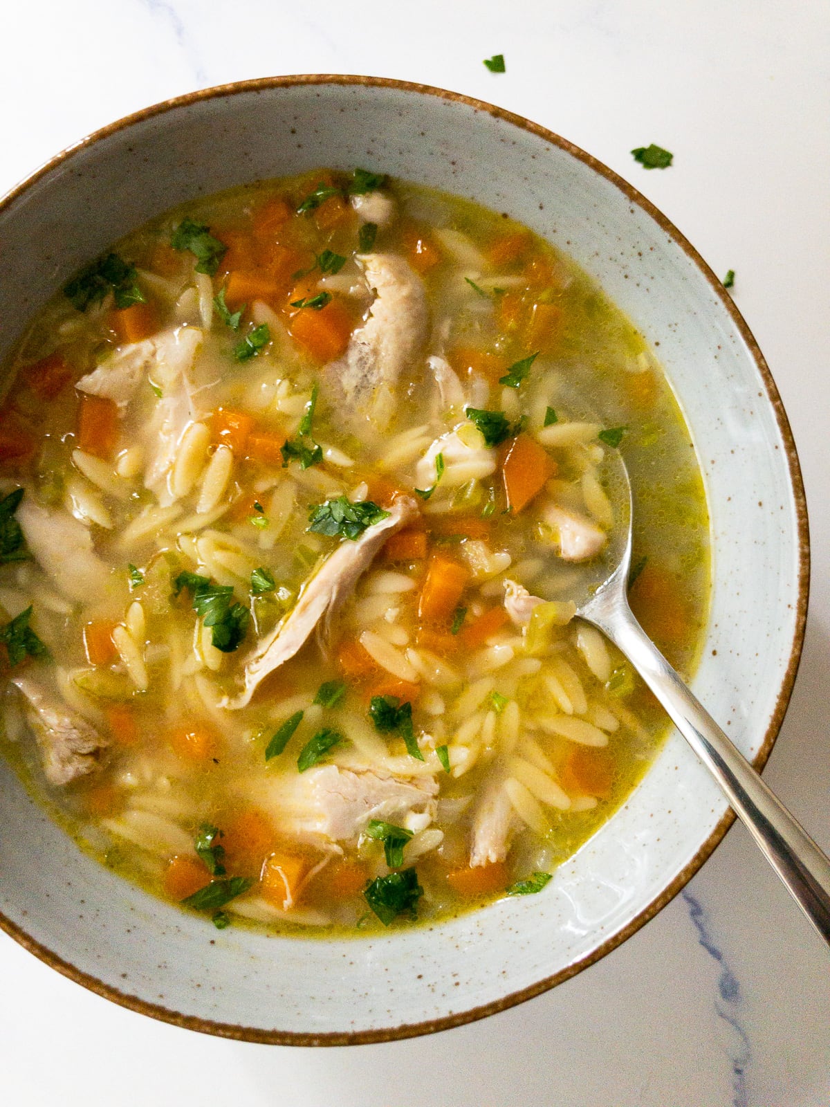 lemon chicken orzo soup garnished with parsley in a bowl with a spoon