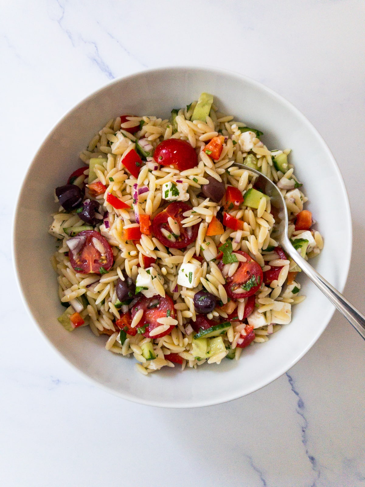 greek orzo salad in a white bowl with a spoon