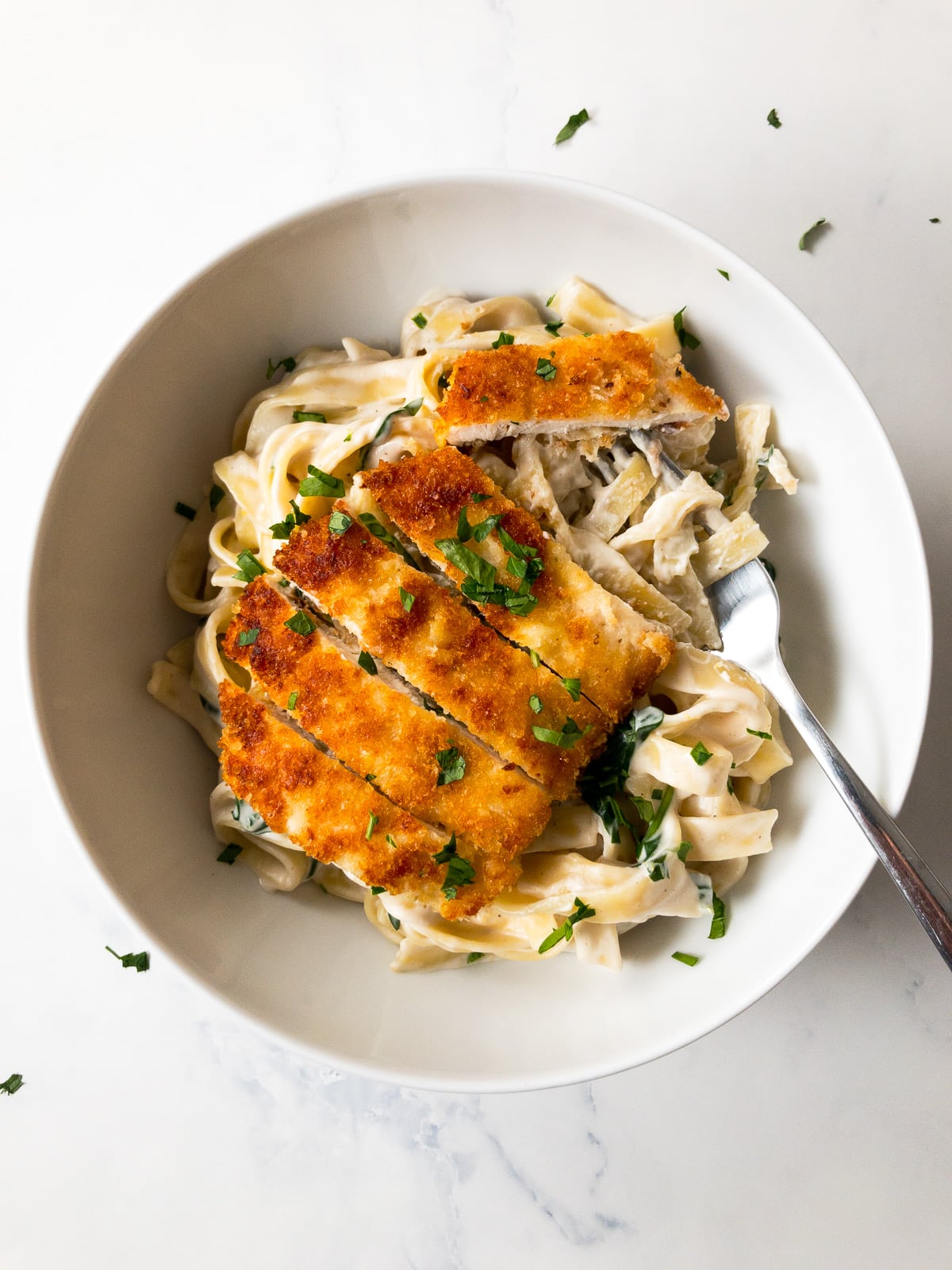 lemon chicken pasta garnished with parsley in a white bowl with a fork
