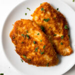 parmesan crusted chicken garnished with chopped parsley on a white plate