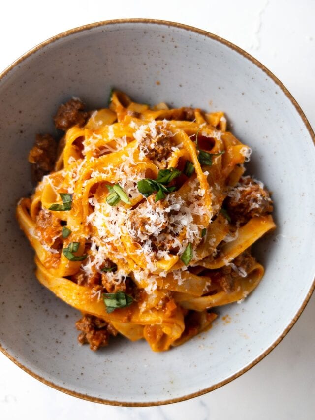 creamy fettuccine bolognese garnished with parmesan cheese and fresh basil leaves in a bowl