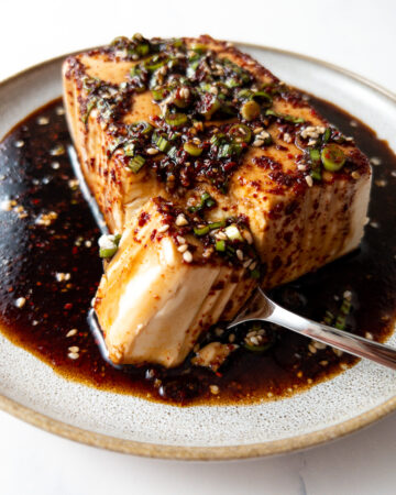 silken tofu covered in a garlic soy sauce on a plate with a spoon