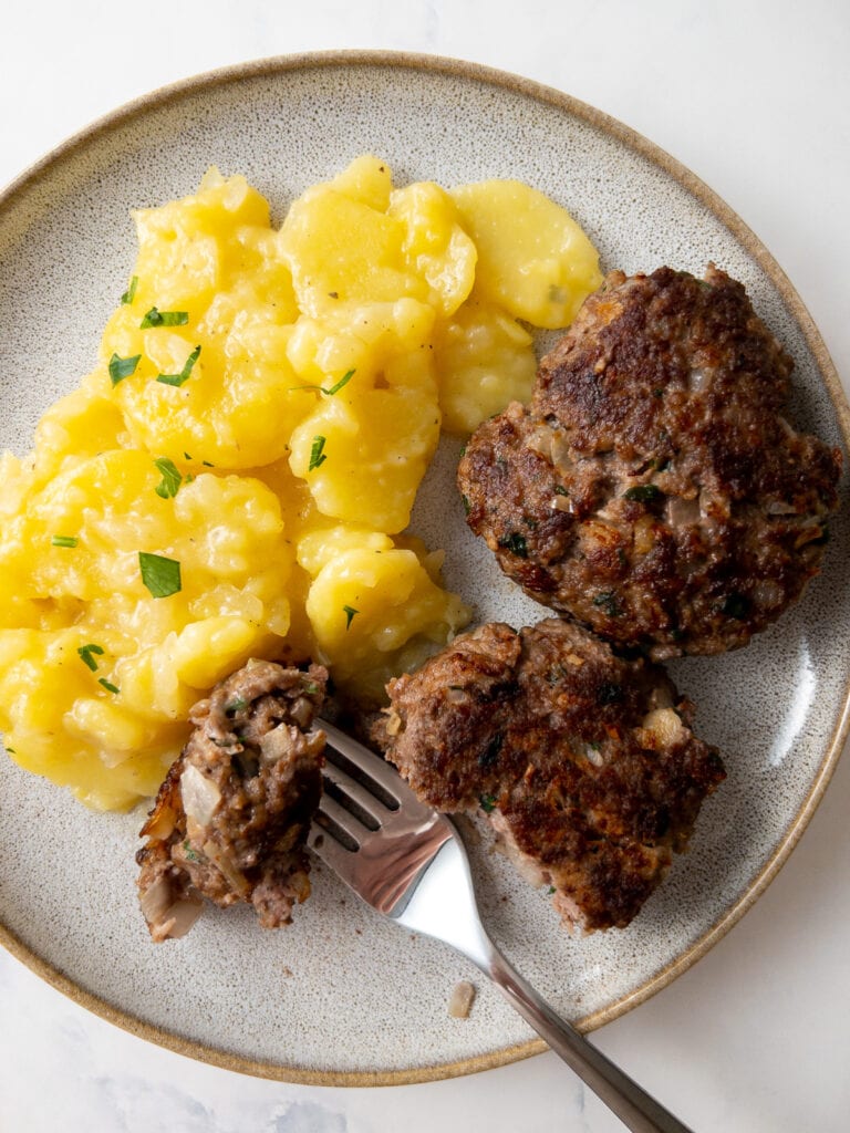 Frikadellen on a plate with German potato salad and a fork