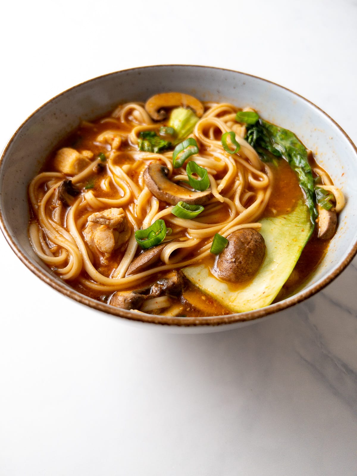 spicy chicken udon noodle soup garnished with green onions in a bowl