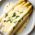 white asparagus with hollandaise sauce garnished with parsley on a plate