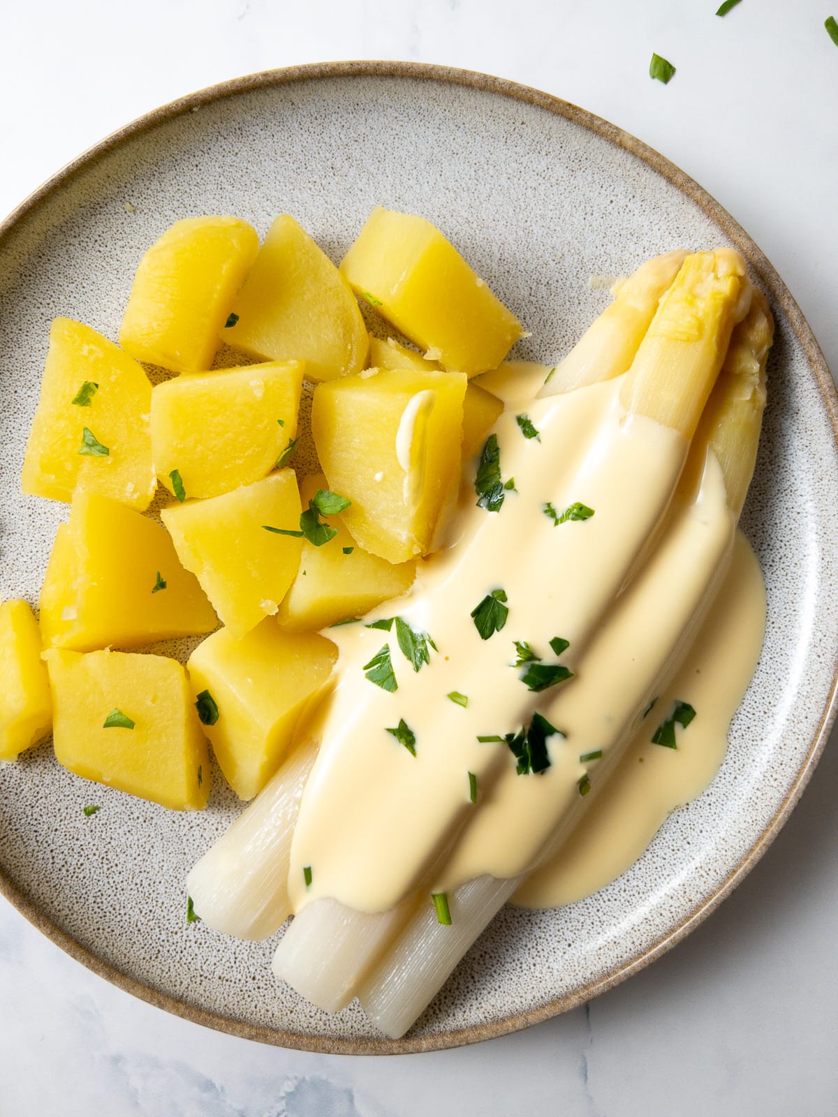 white asparagus with cooked potatoes and hollandaise sauce garnished with parsley on a plate