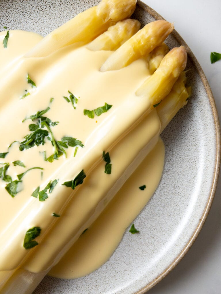 white asparagus with hollandaise sauce garnished with parsley on a plate