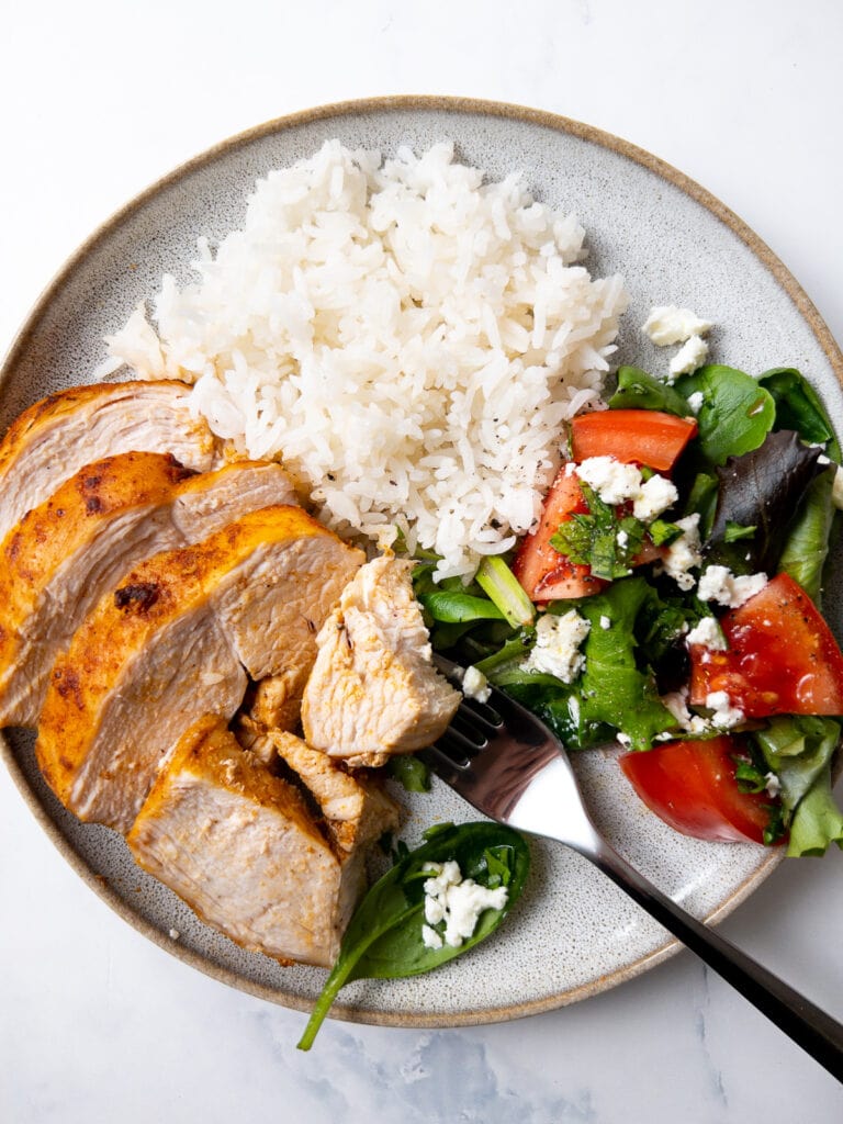 air fryer chicken breast slices served with white rice and a side salad on a plate with a fork