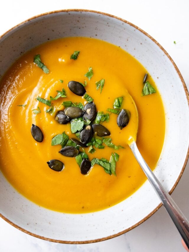 sweet potato butternut squash soup topped with parsley and pumpkin seeds in a bowl with a spoon
