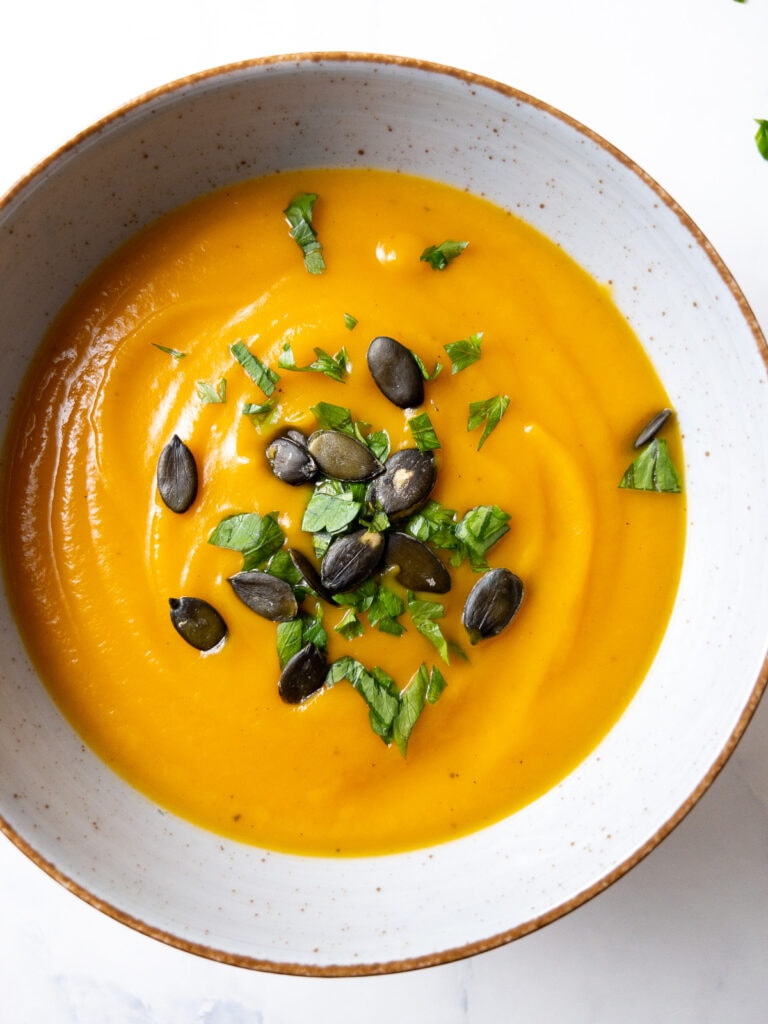 sweet potato butternut squash soup topped with parsley and pumpkin seeds in a bowl