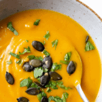 sweet potato butternut squash soup in a bowl with a spoon garnished with parsley and pumpkin seeds