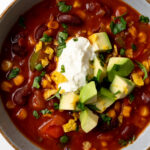 vegetarian chili garnished with avocado dices, sour cream, chopped cilantro, and tortilla chips in a bowl