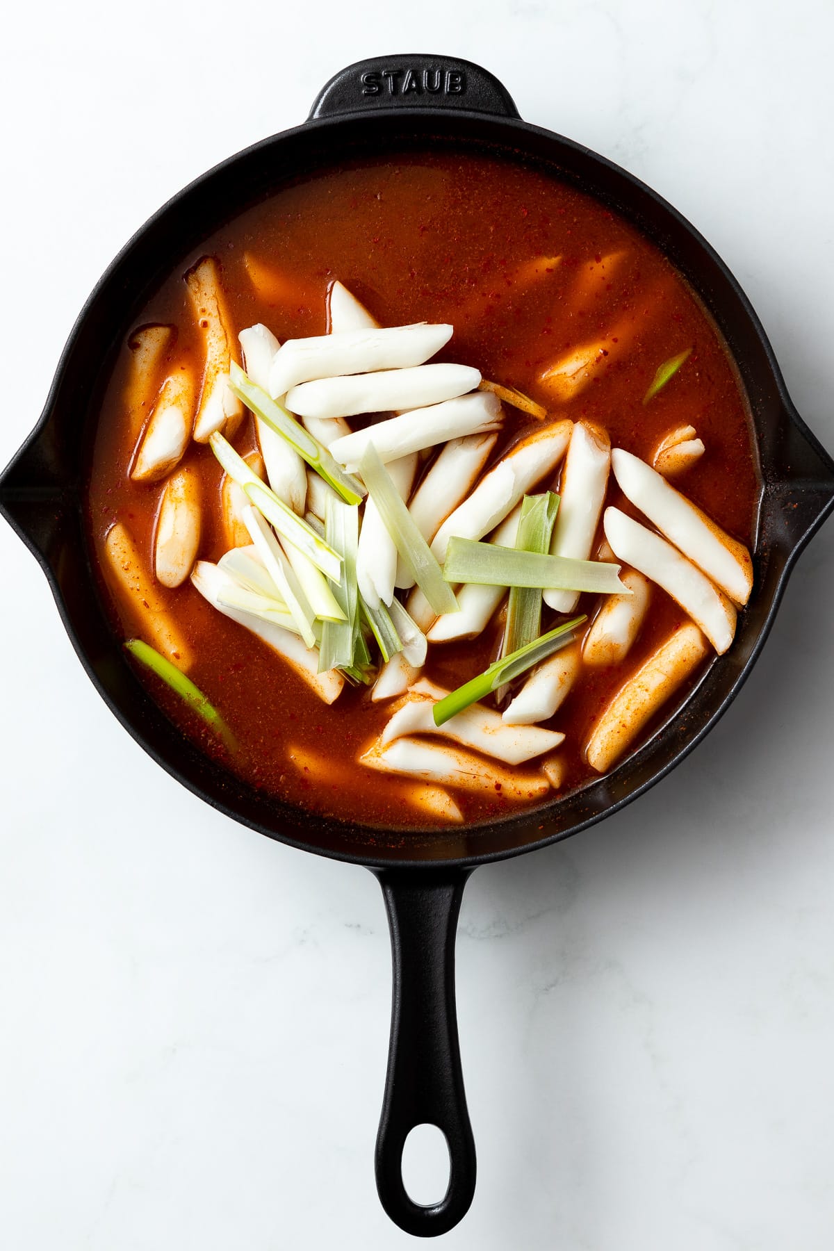 tteokbokki sauce in a pan with uncooked rice cakes and green onions