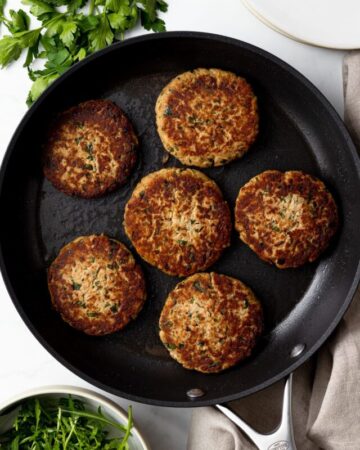 six tuna patties in a pan with plates and arugula on a table