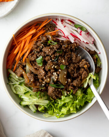 ground beef bulgogi with julienned carrots, radishes, cucumber, and salad served over rice in a bowl with a spoon