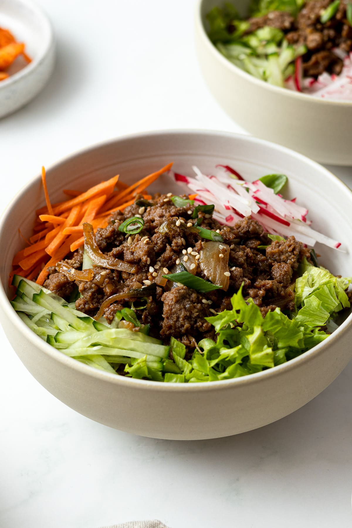 ground beef bulgogi with julienned carrots, radishes, cucumber, and salad served over rice in a bowl
