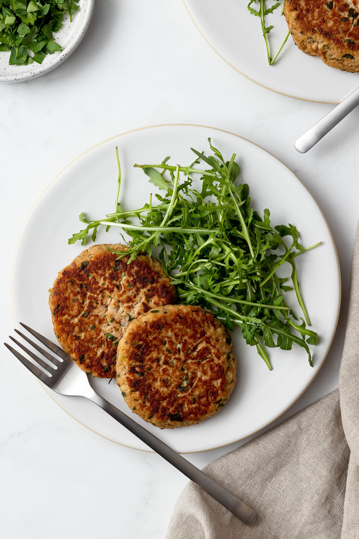 two plates of two tuna patties with some arugula and a fork