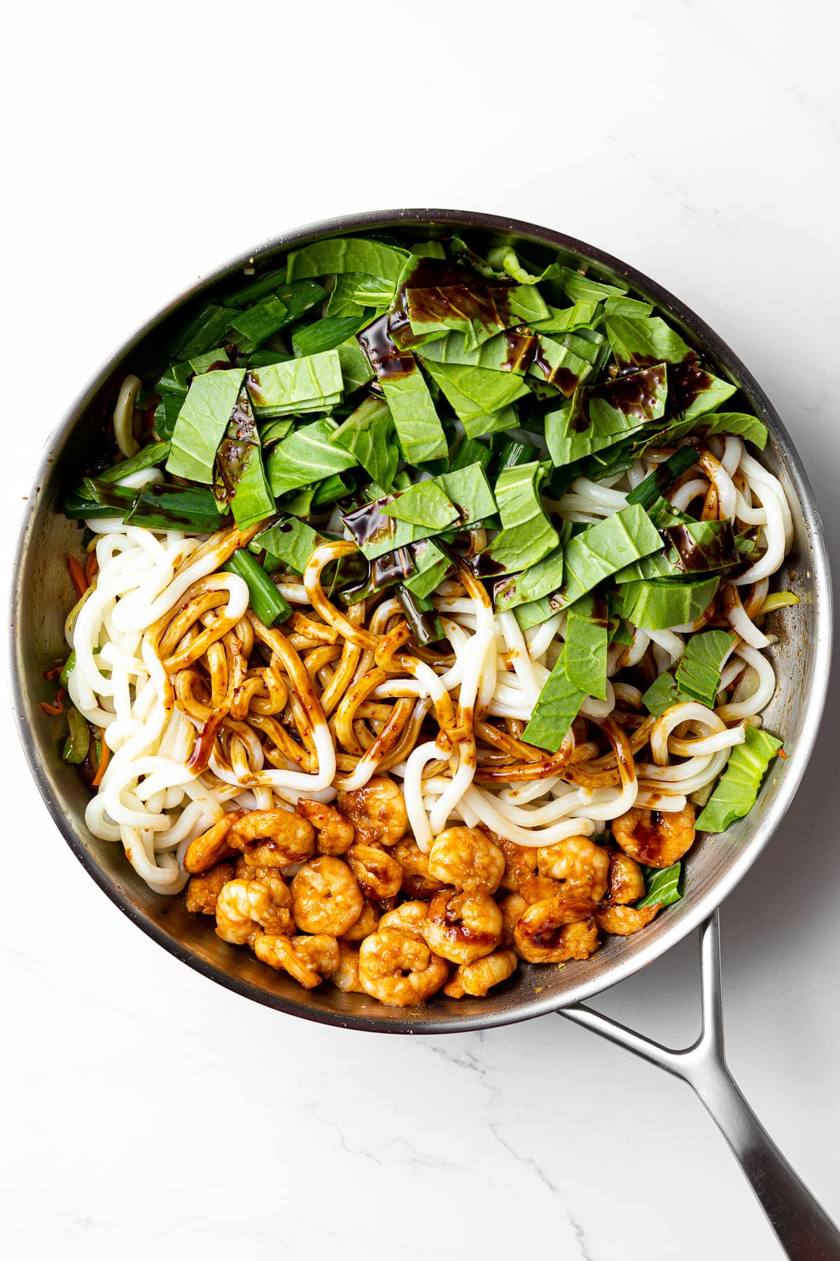 udon noodles, seared shrimp, choppedd bok choy, and stir fry sauce in a pan