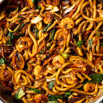 shrimp udon stir fry noodles garnished with sesame seeds in a pan on a table