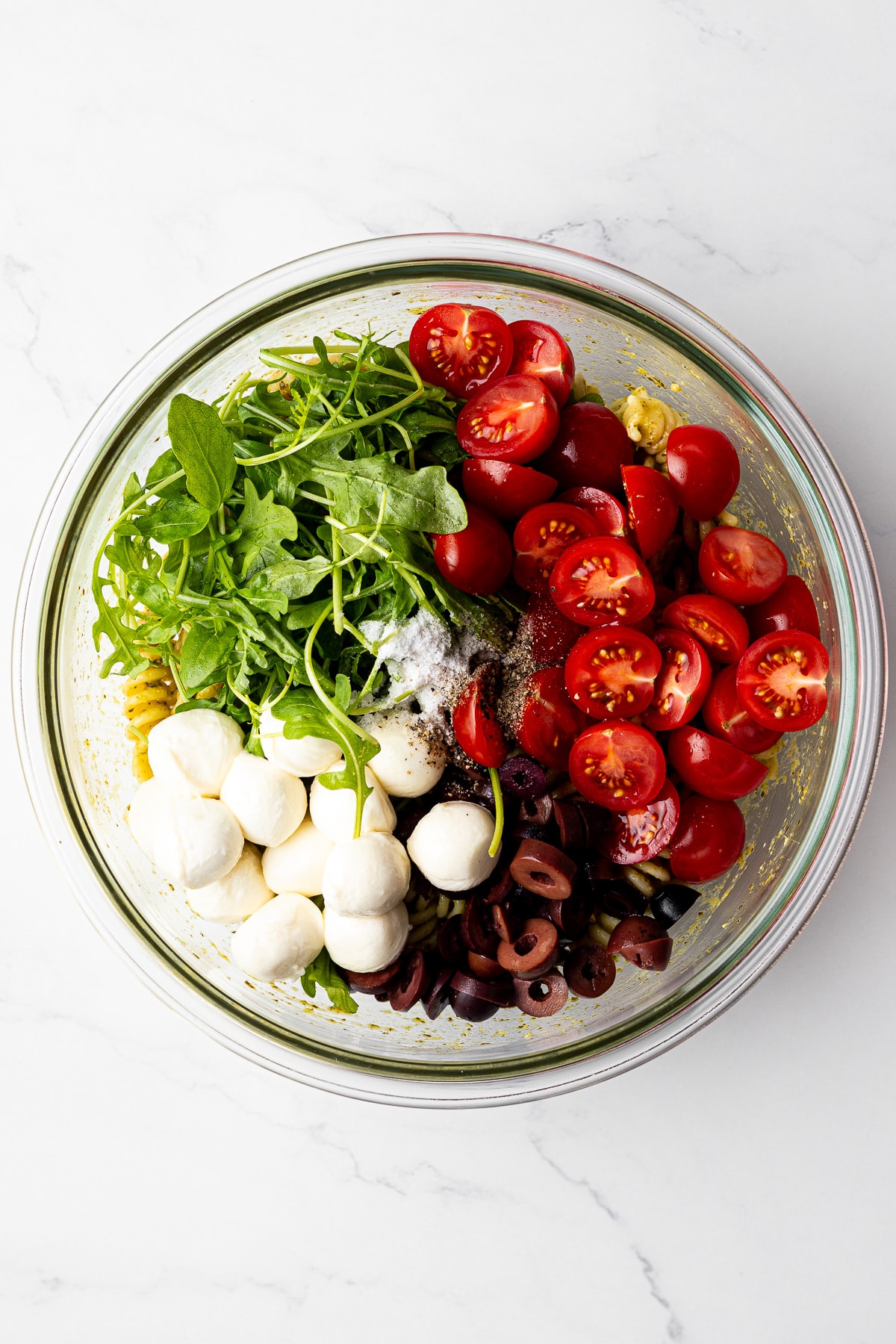 all pesto caprese pasta salad ingredients in a bowl before mixing everything