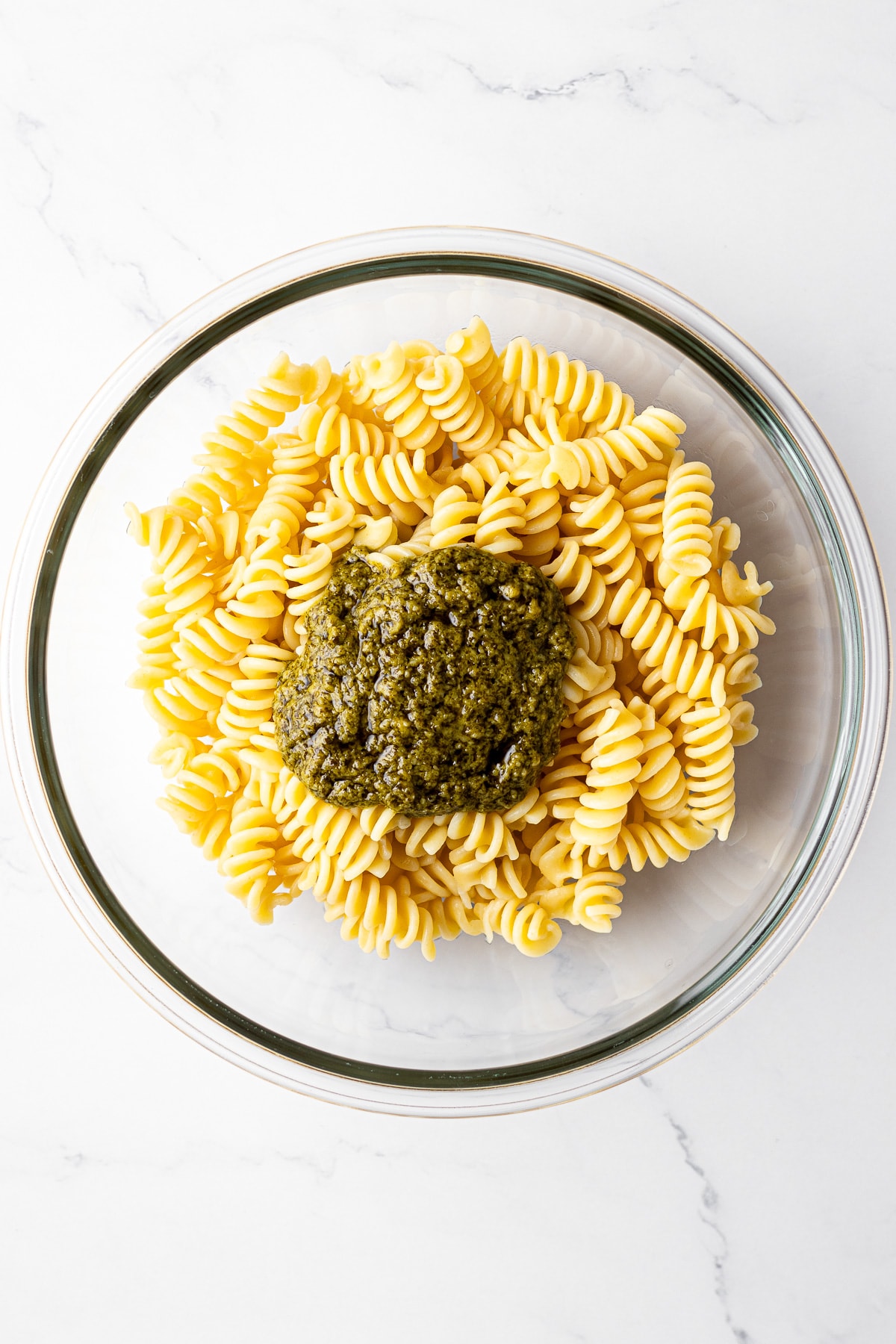cooked pasta and basil pesto in a mixing bowl