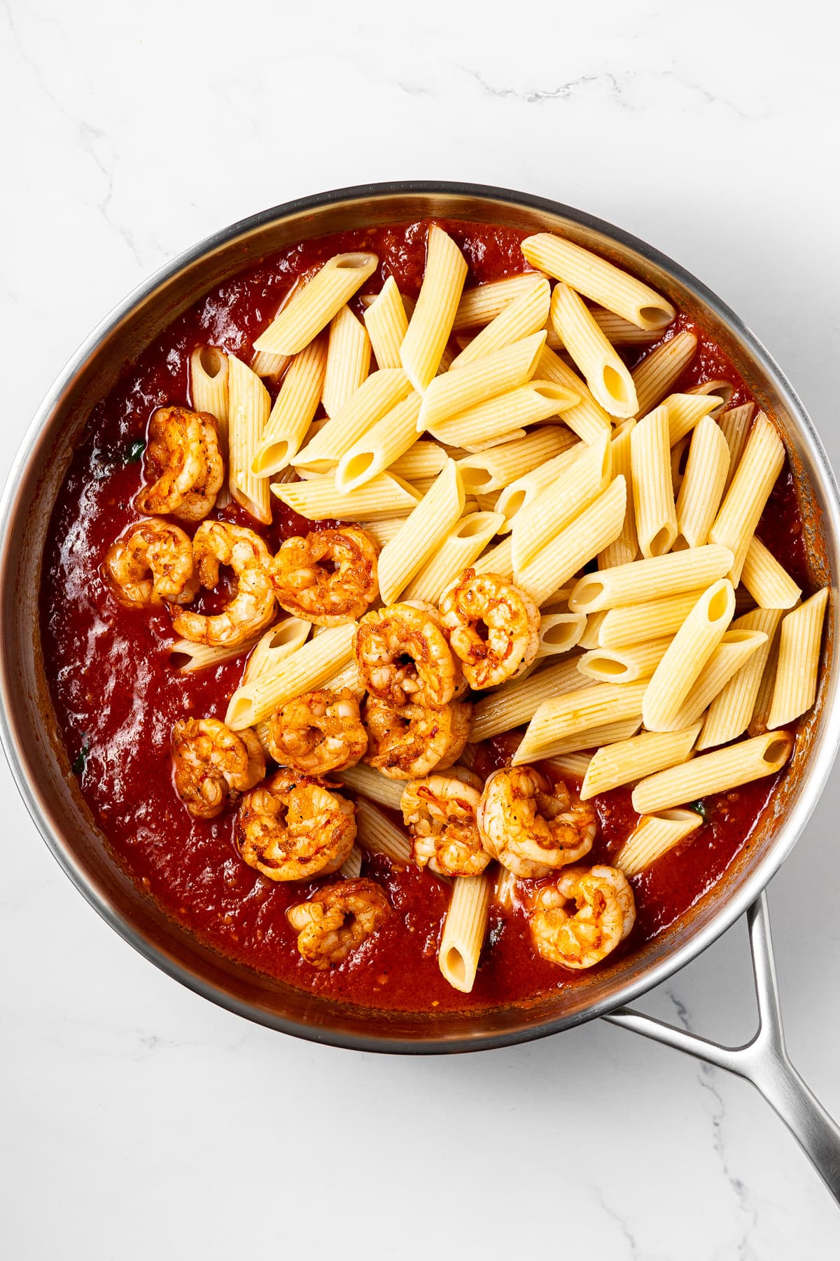 shrimp arrabbiata sauce, cooked shrimp, and cooked penne pasta in a pan