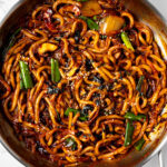 kimchi udon in a pan garnished with chopped roasted seaweed and sesame seeds