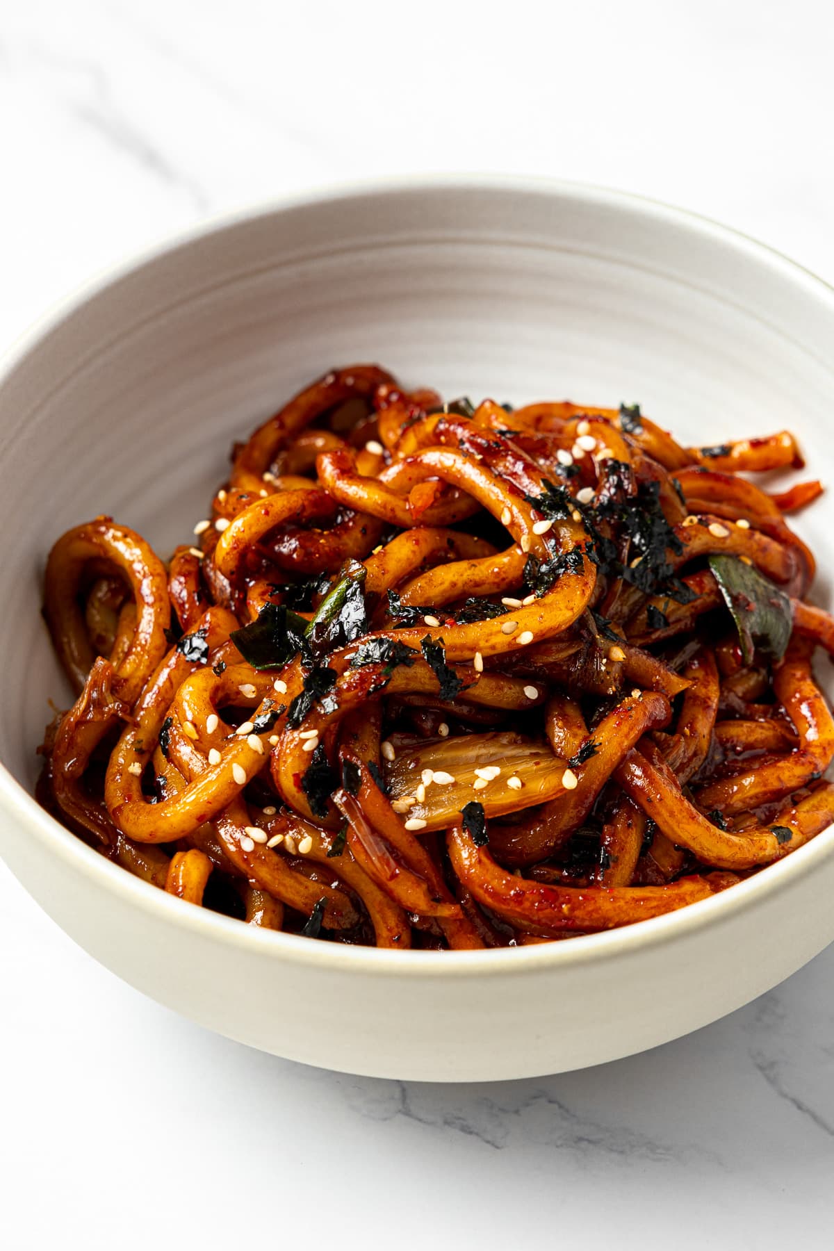 kimchi udon in a bowl garnished with chopped roasted seaweed and sesame seeds