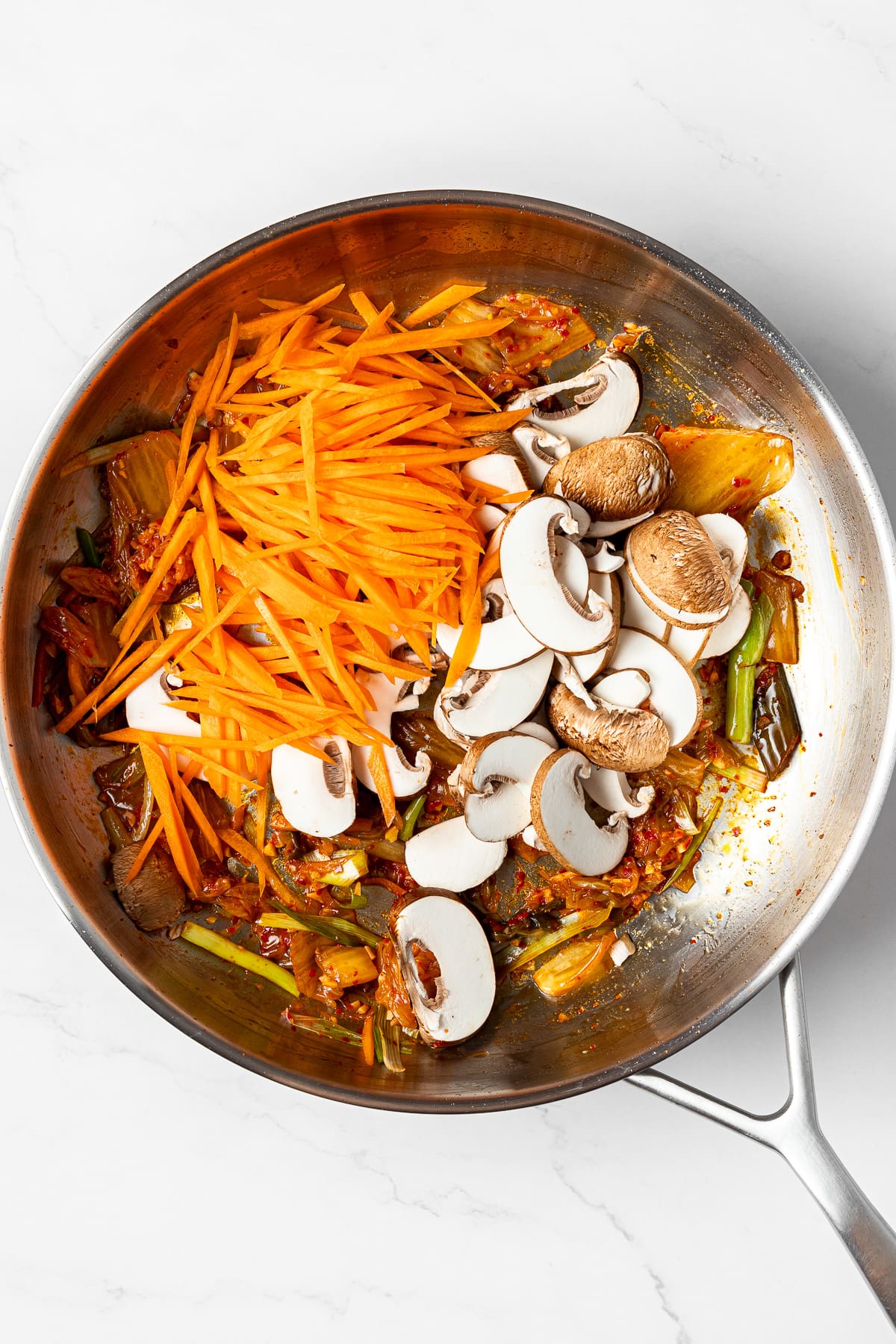 sautéed aromatics, kimchi, mushrooms, and julienned carrots in a pan