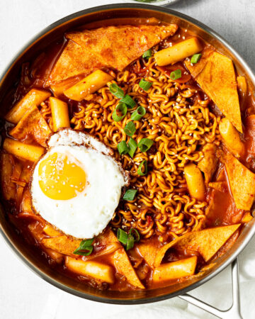 korean rabokki garnished with sesame seeds, green onion, and a fried egg in a pan