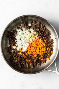 cooked ground beef in a pan with chopped carrots, onions, and garlic added