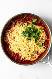 meat sauce in a pan with spaghetti and fresh basil added