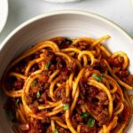 spaghetti with meat sauce in a bowl garnished with chopped basil