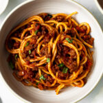 spaghetti with meat sauce in a bowl garnished with chopped basil