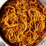 spaghetti with meat sauce in a pan garnished with chopped basil and chopped basil and red pepper flakes in two small bowl on the table